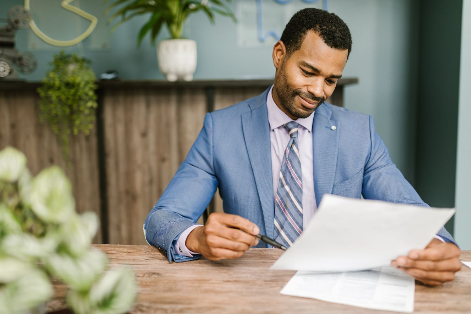 Professional business agent in a blue suit smiling while reviewing and signing partnership paperwork at a desk, conveying enthusiasm and trustworthiness