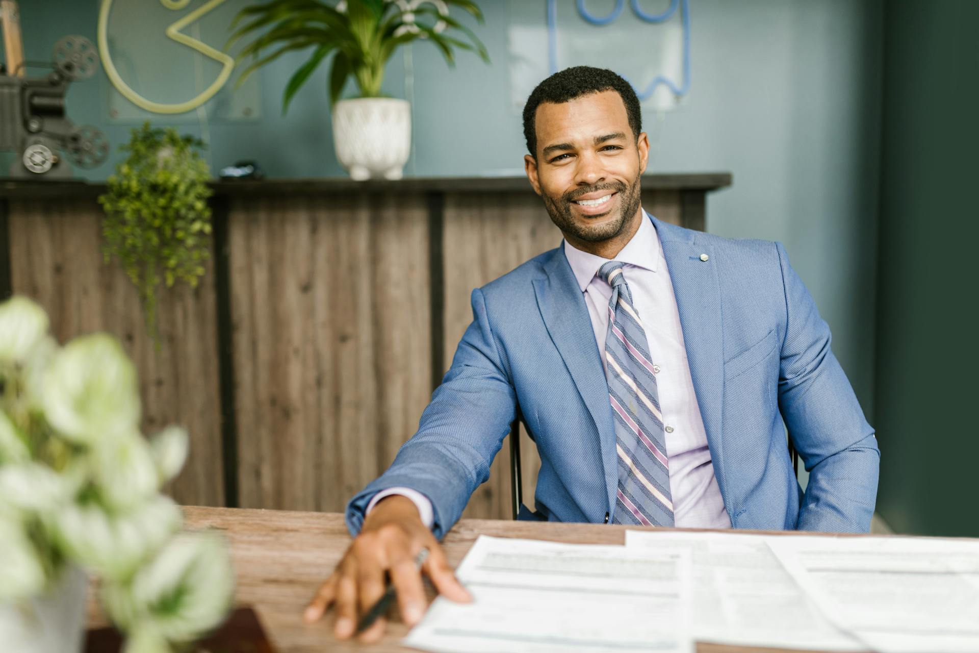 Confident businessman in corporate attire smiling at his desk in a modern office setting.