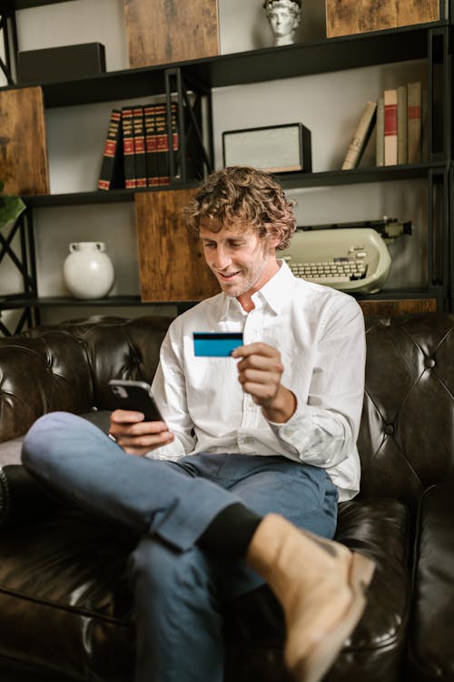 Man Looking At His Cellphone and  Holding A Bank Card                                             