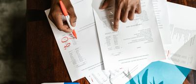 Overhead view of a person using a red marker to circle numbers on a printed consolidated statement of financial position.