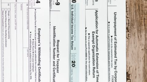 Close-up of various U.S. tax forms including W-4, W-9, and 1040 on a rustic wooden surface.