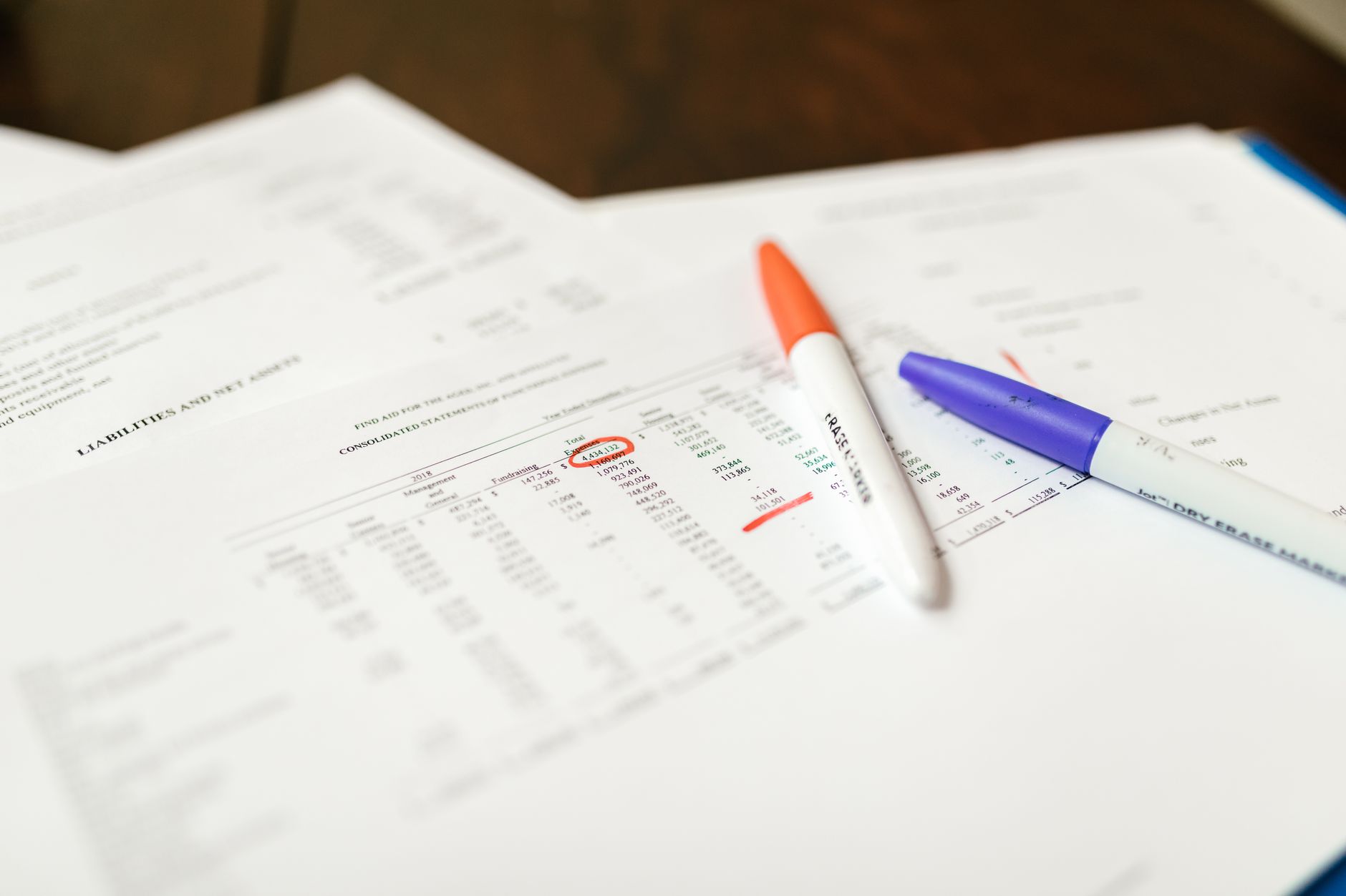 Printed financial documents marked up with pens and circled figures, comparing numbers from two offers side by side