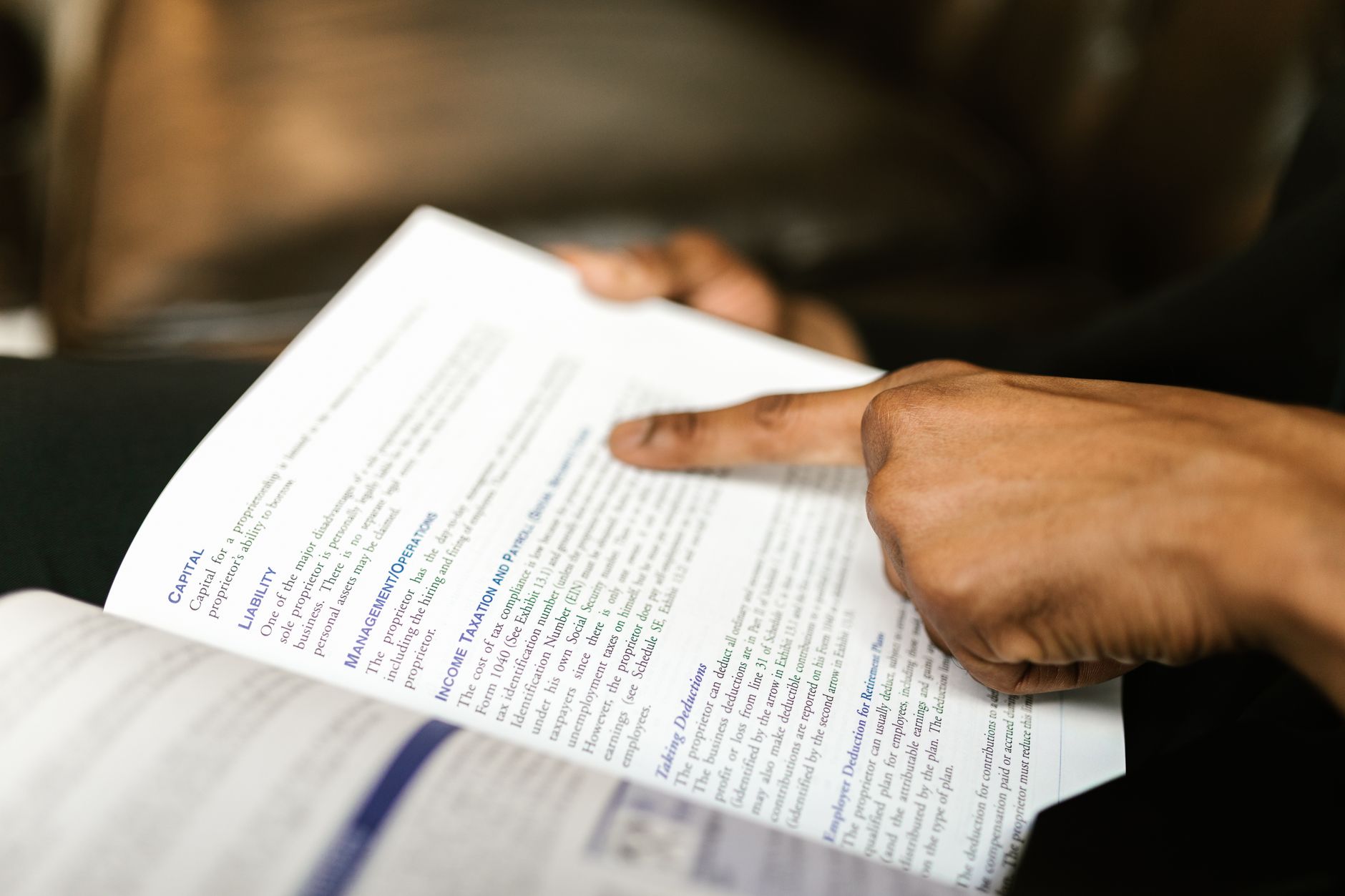 A person points to text in a book, highlighting finance content.