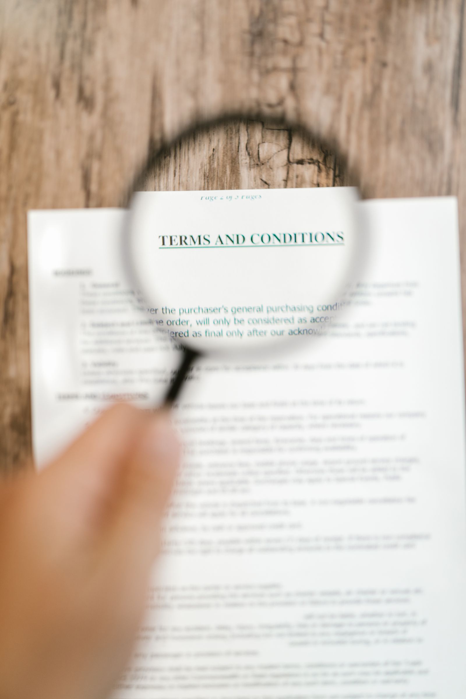 A hand holds a magnifying glass over the heading of a printed terms and conditions page