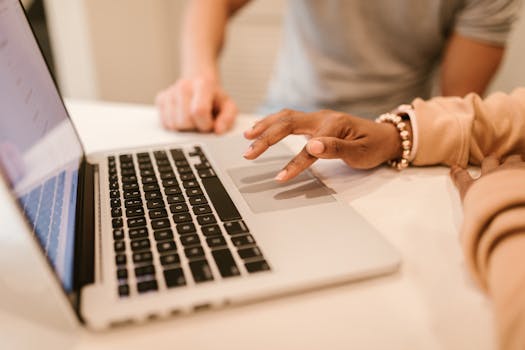 Two people working together on a laptop, focusing on hands near touchpad and keyboard.