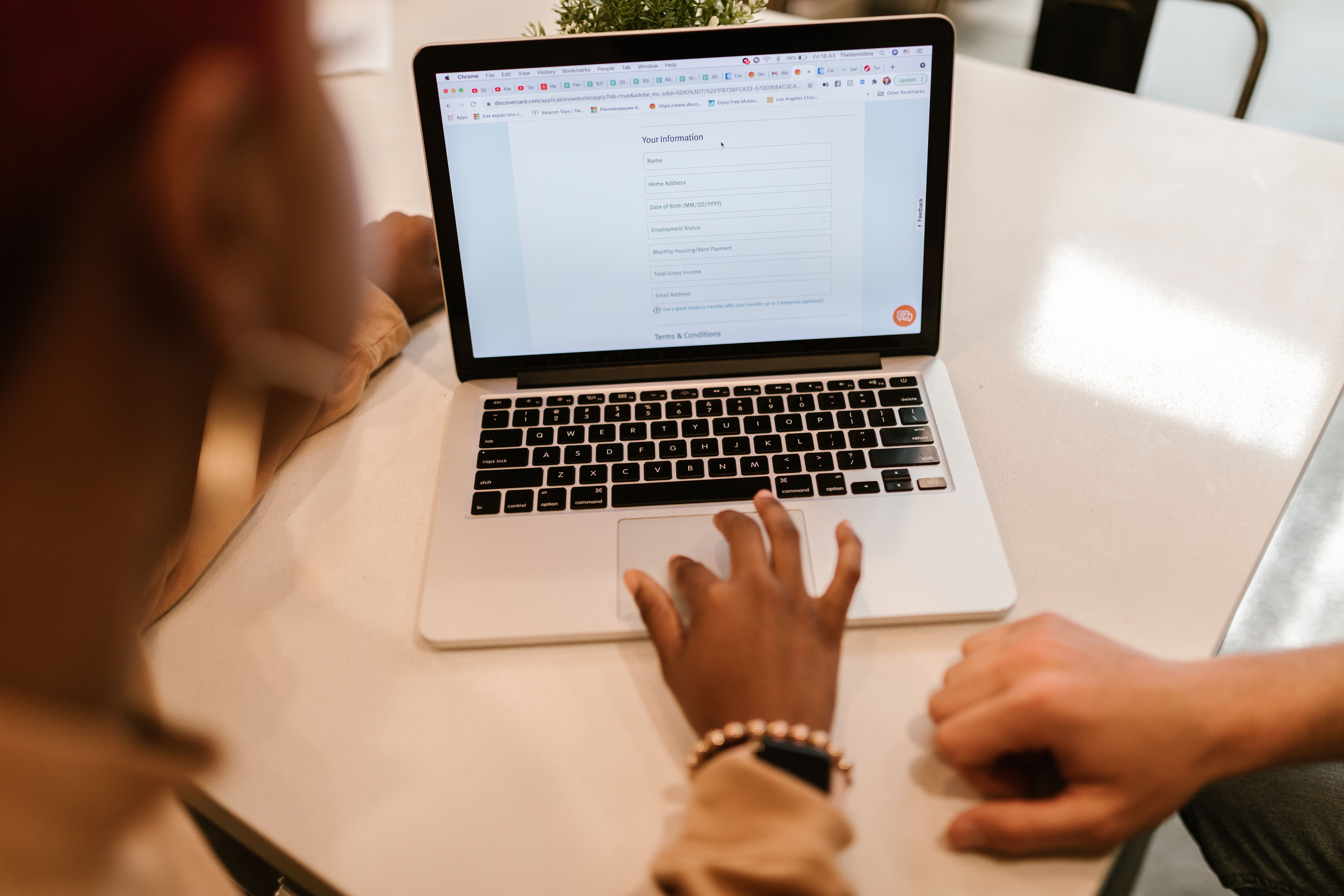 Two people review and complete an online form on a laptop at a table