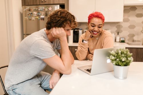 Free Smiling couple enjoying time together using a laptop in a bright modern kitchen. Stock Photo