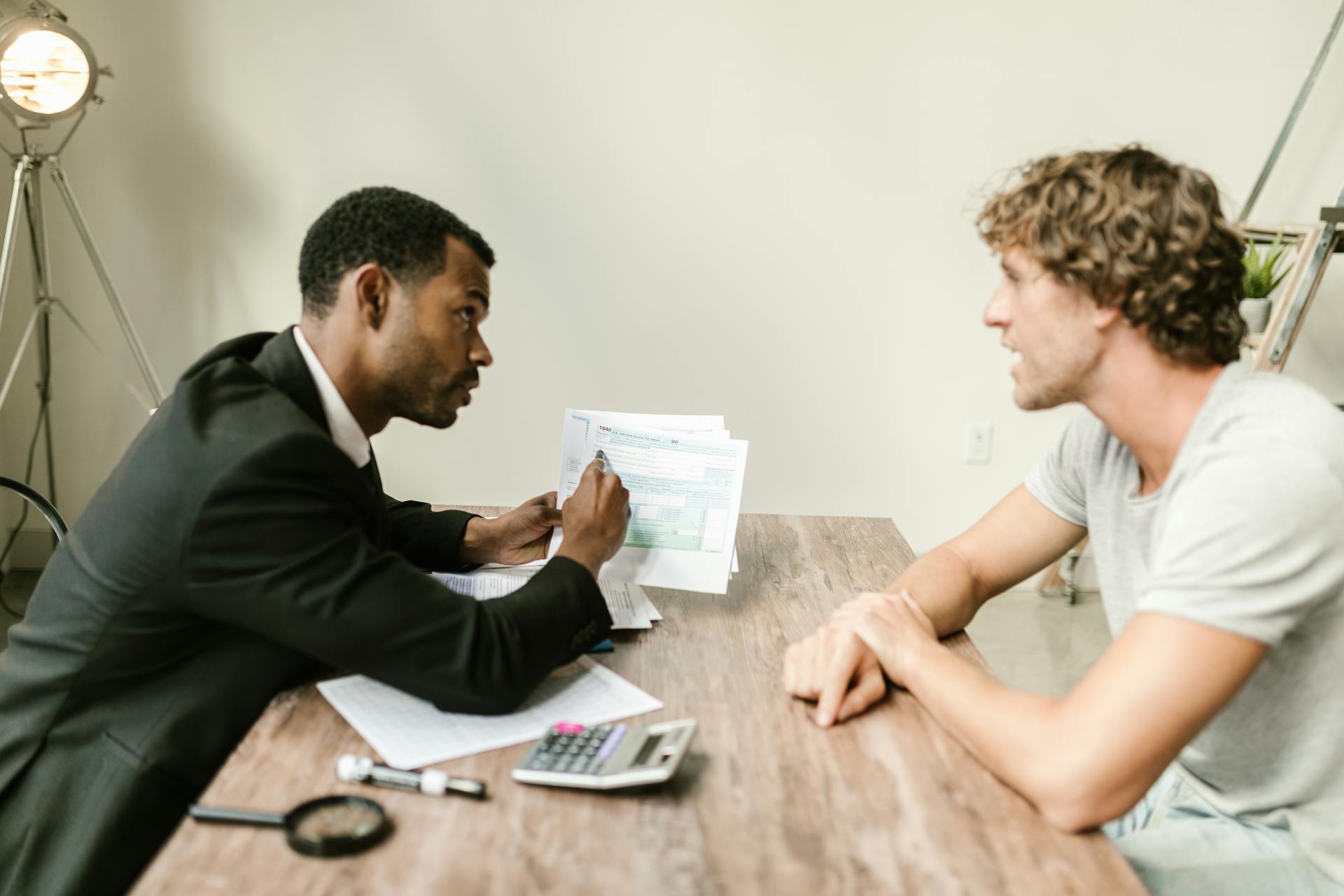 A financial advisor discusses paperwork with a client at a desk in a modern office.