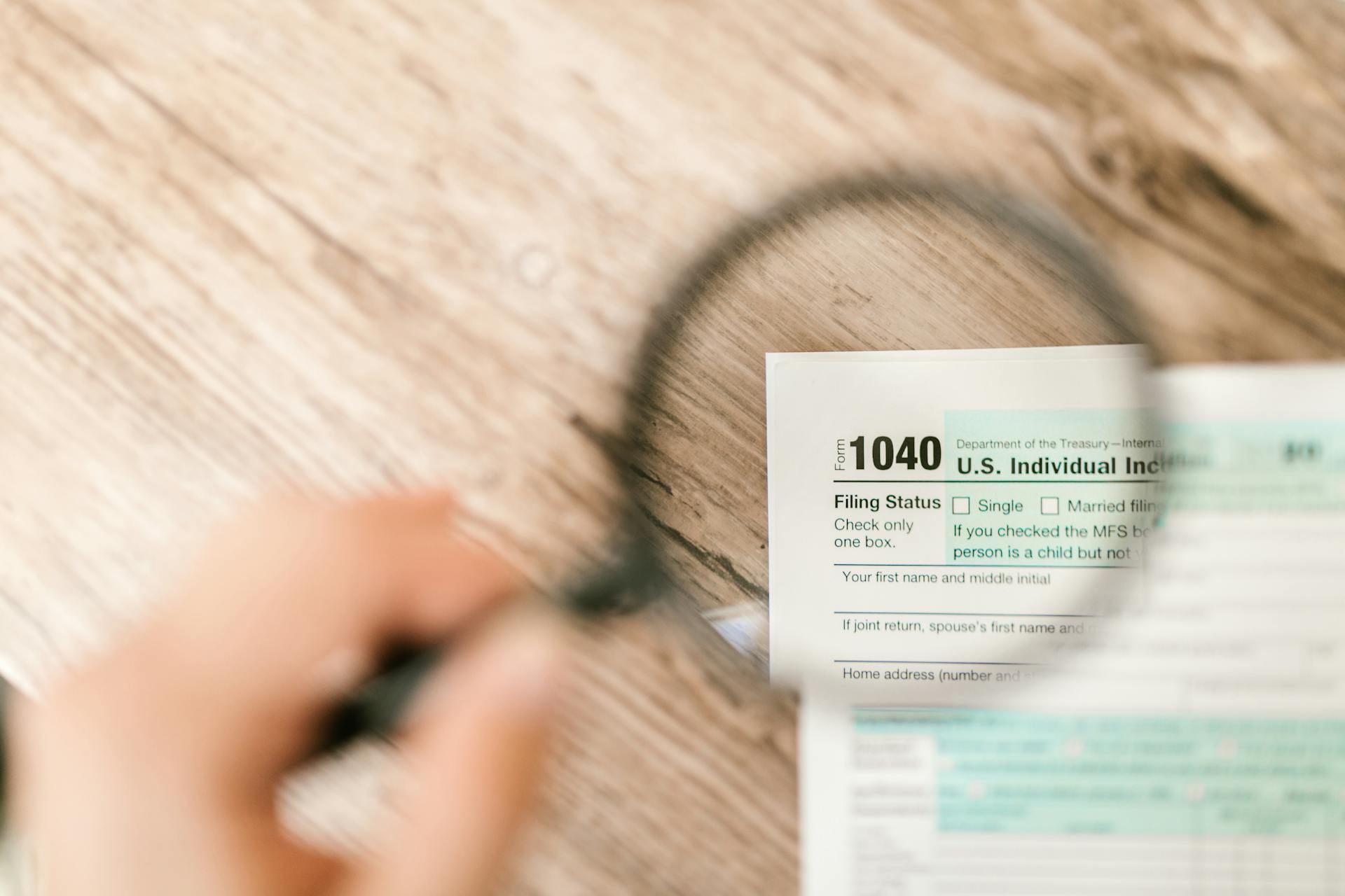 Close-up image of IRS Form 1040 under a magnifying glass on a wooden surface.