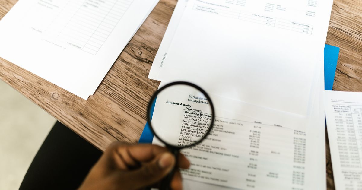 Une main tient une loupe au-dessus d'un document imprimé posé sur un bureau.