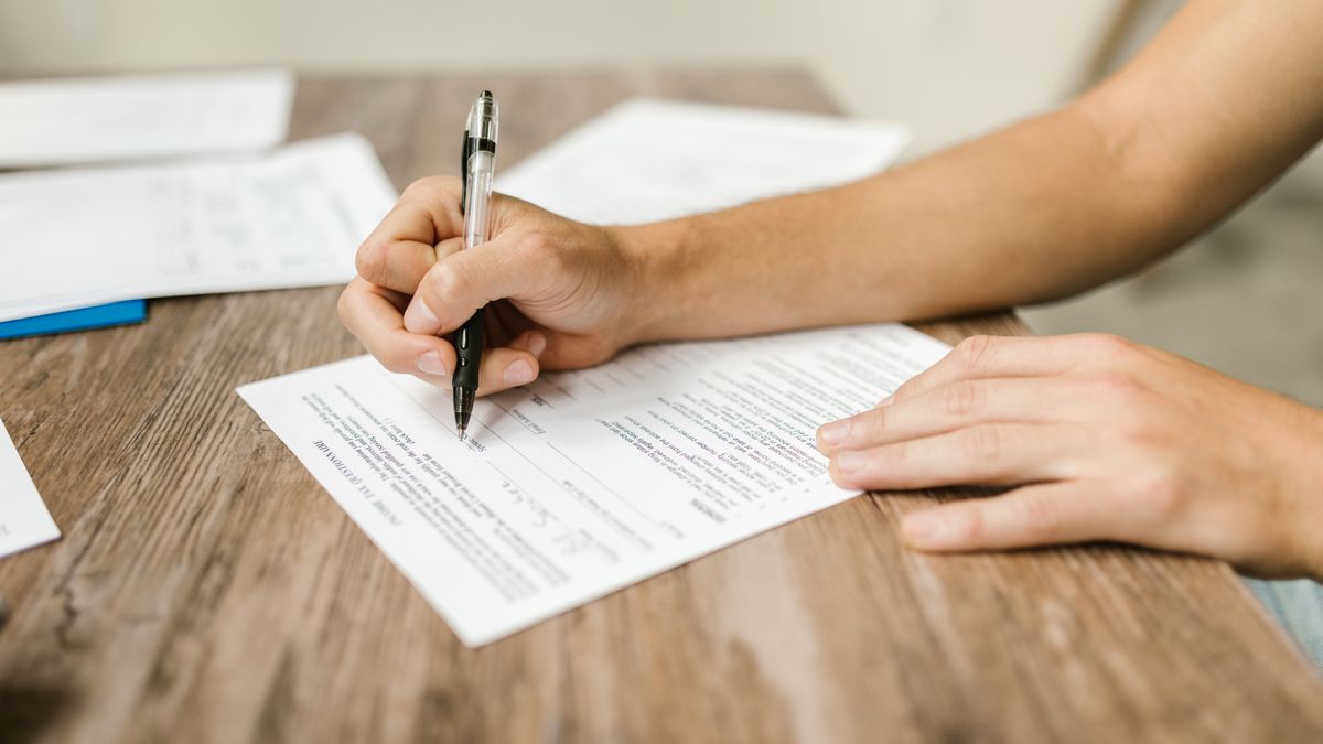 Hand filling out paperwork with a pen, showcasing focus on document completion.