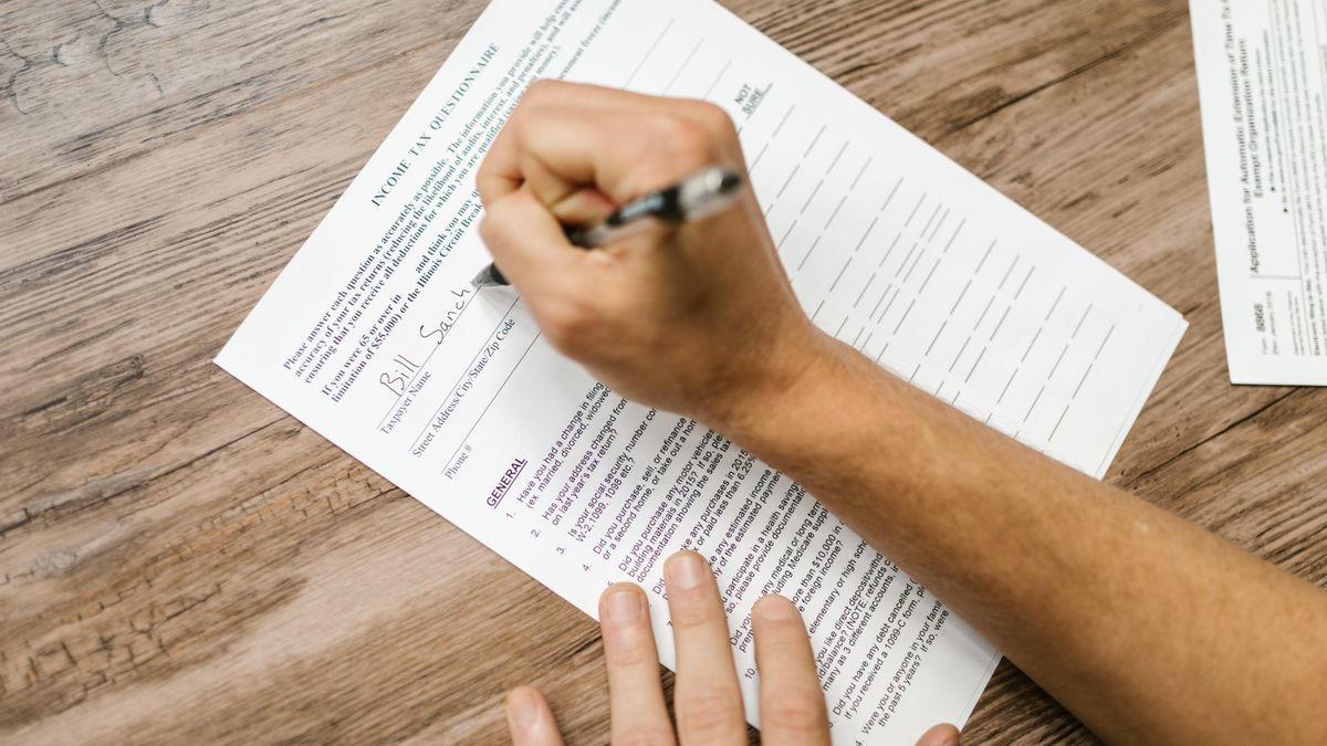 Person filling out a tax questionnaire with a pen, showing close-up on wooden table.