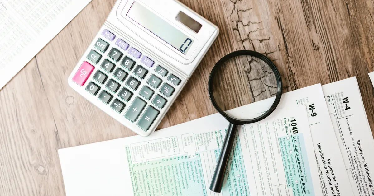A calculator and a magnifying glass on top of tax forms on a wooden desk, representing AI register template