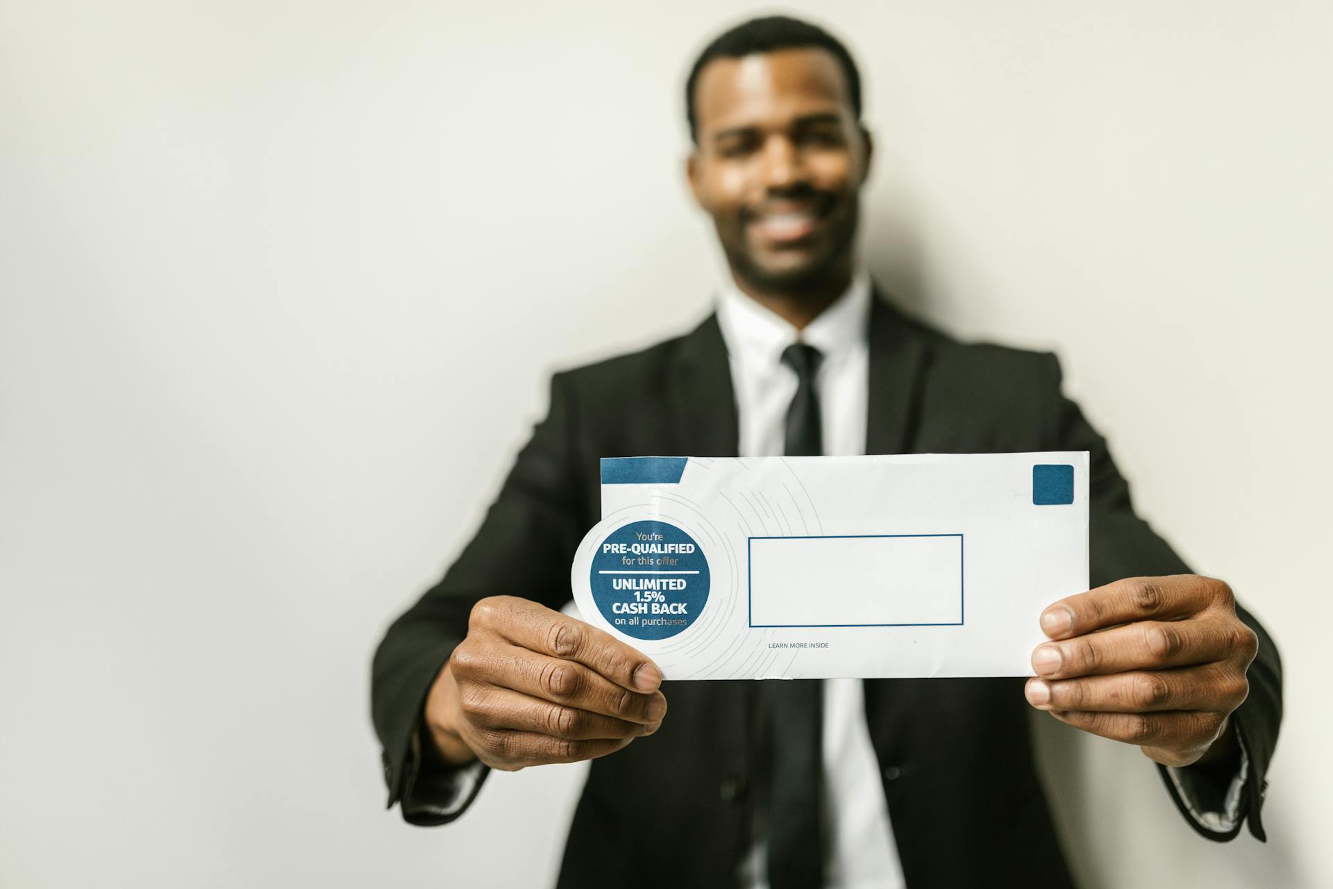 Smiling man in suit holding a cash back promotional envelope with selective focus.