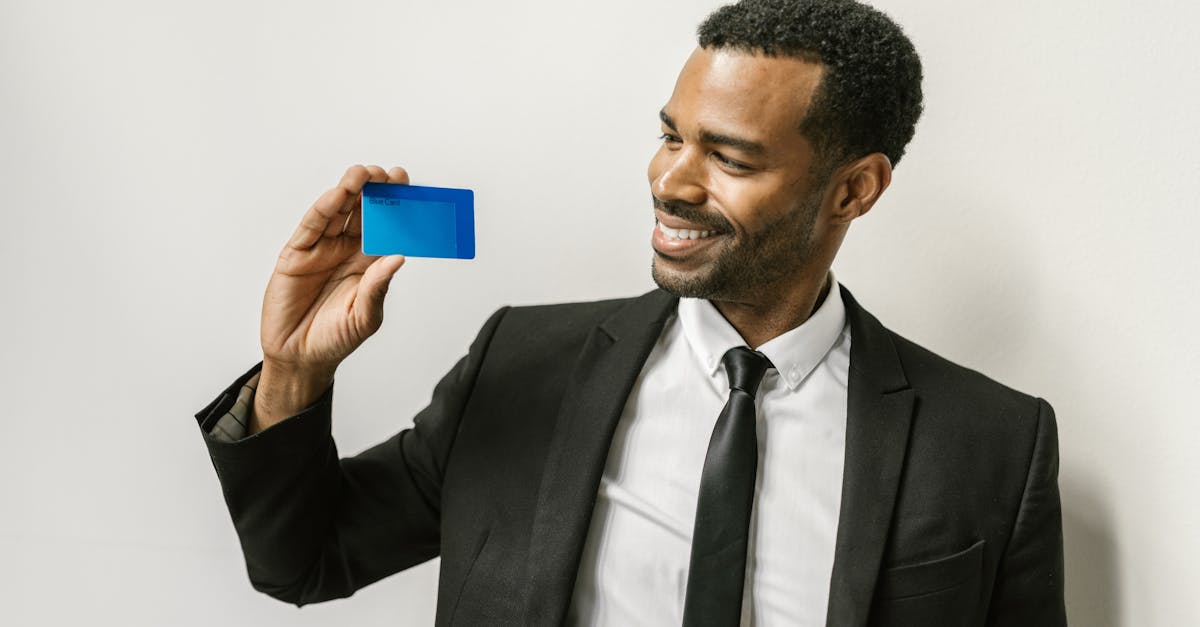 A confident man in a suit holds a credit card, smiling towards it.