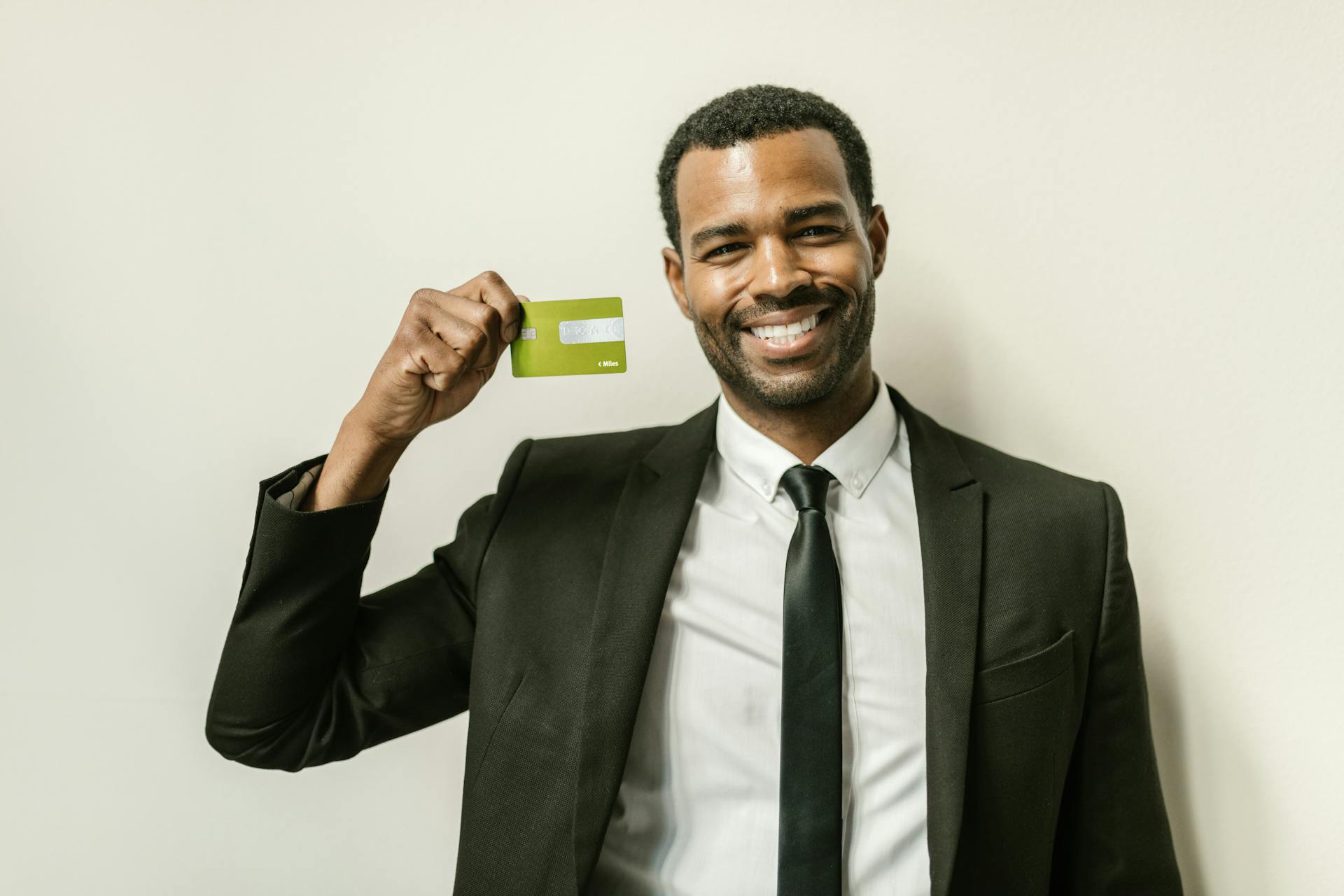 Smiling businessman in a suit displaying a green credit card indoors.