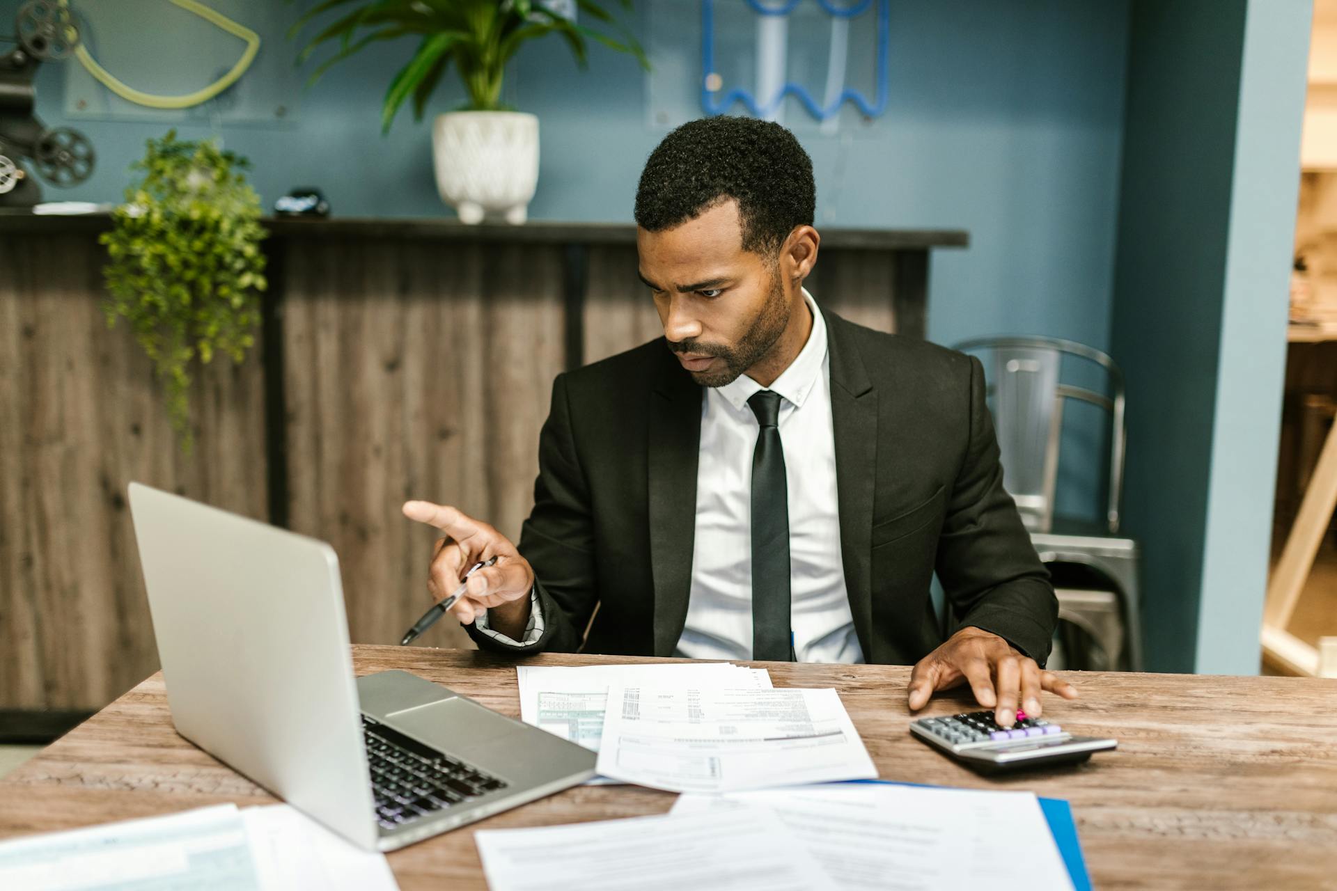 Professional man in a suit using a laptop and calculator in an office setting.