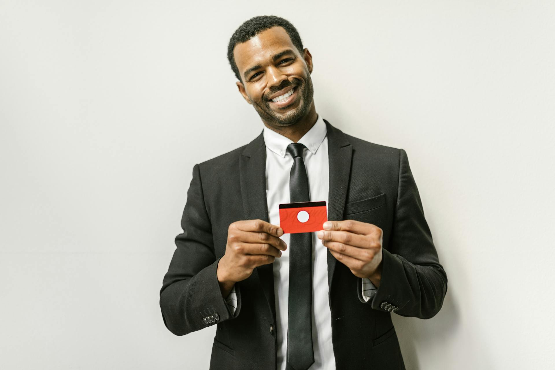 Smiling businessman in a suit holding a red card, posing against a white background.