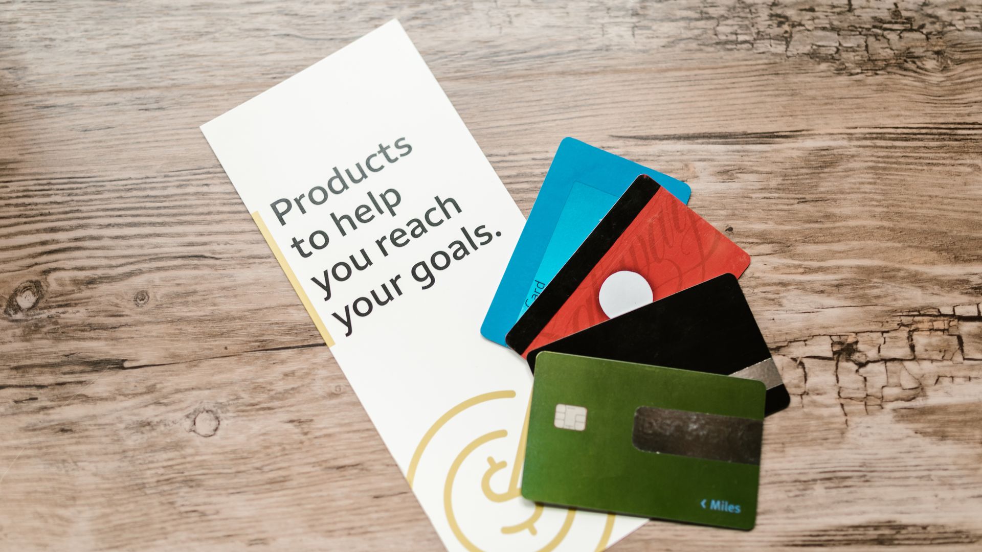 ID Cards: Your Essential Identification Companion 5 Assorted credit cards on a wooden table next to a leaflet with motivational text about financial goals — id cards