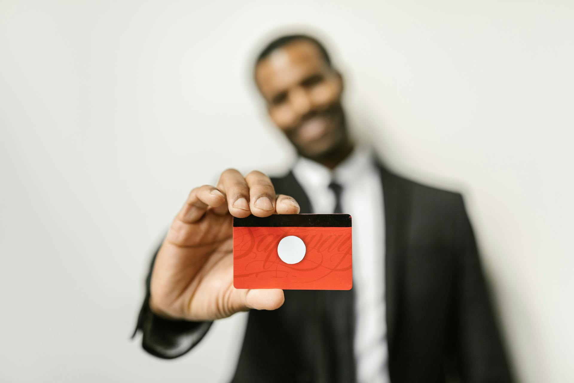 Businessman in formal attire holding a red card, with a focus on the card against a white background.