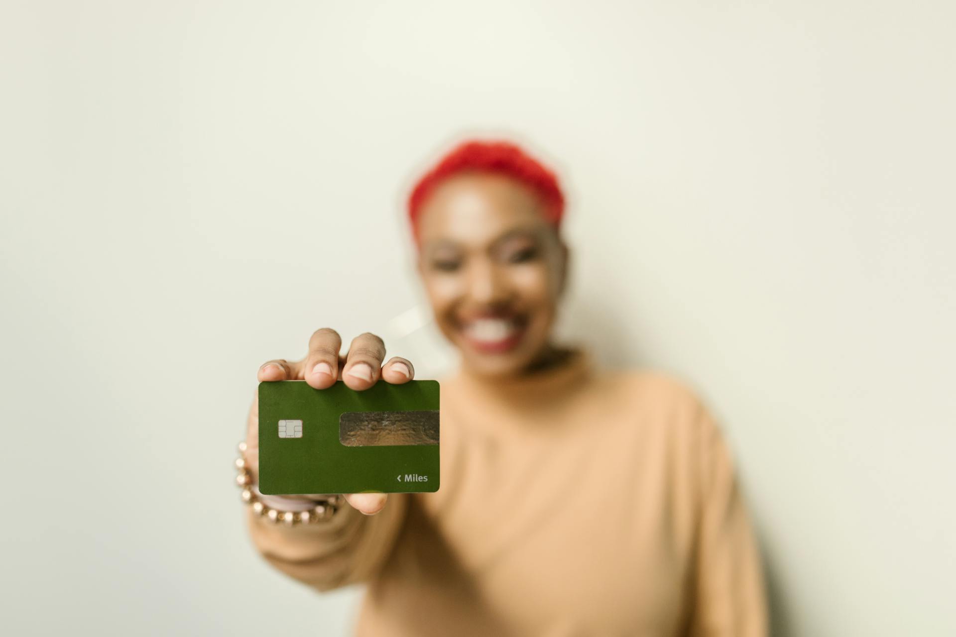 An African American woman smiling while holding out a green credit card.