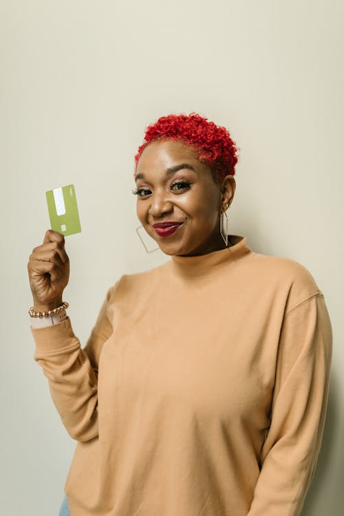 Free A Happy Woman in Brown Sweater Smiling while Holding an ATM Card Stock Photo