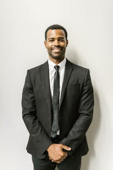 Confident man in formal attire smiling against a plain white wall.
