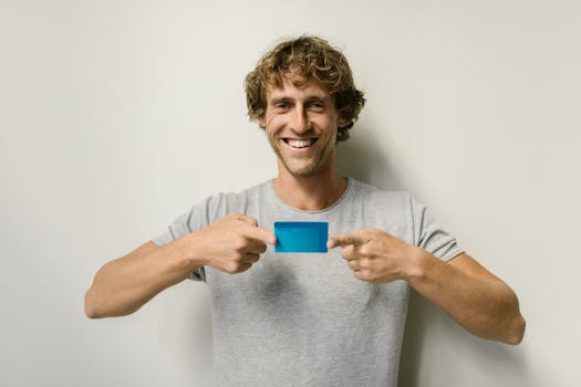Cheerful man holding a blue credit card against a plain white background.
