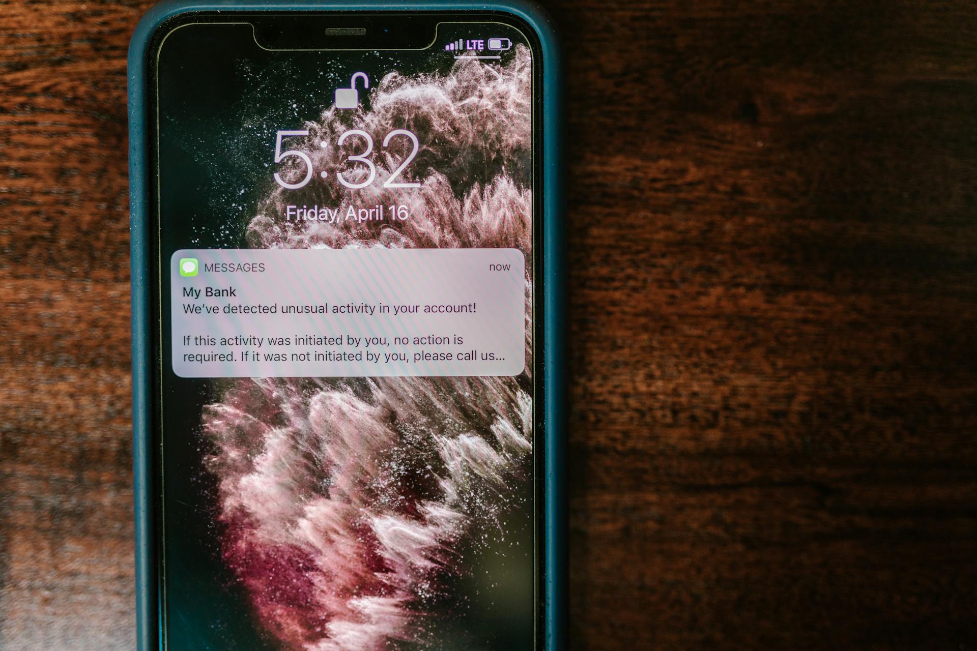 Close-up of a smartphone displaying a bank alert notification on a wooden table.