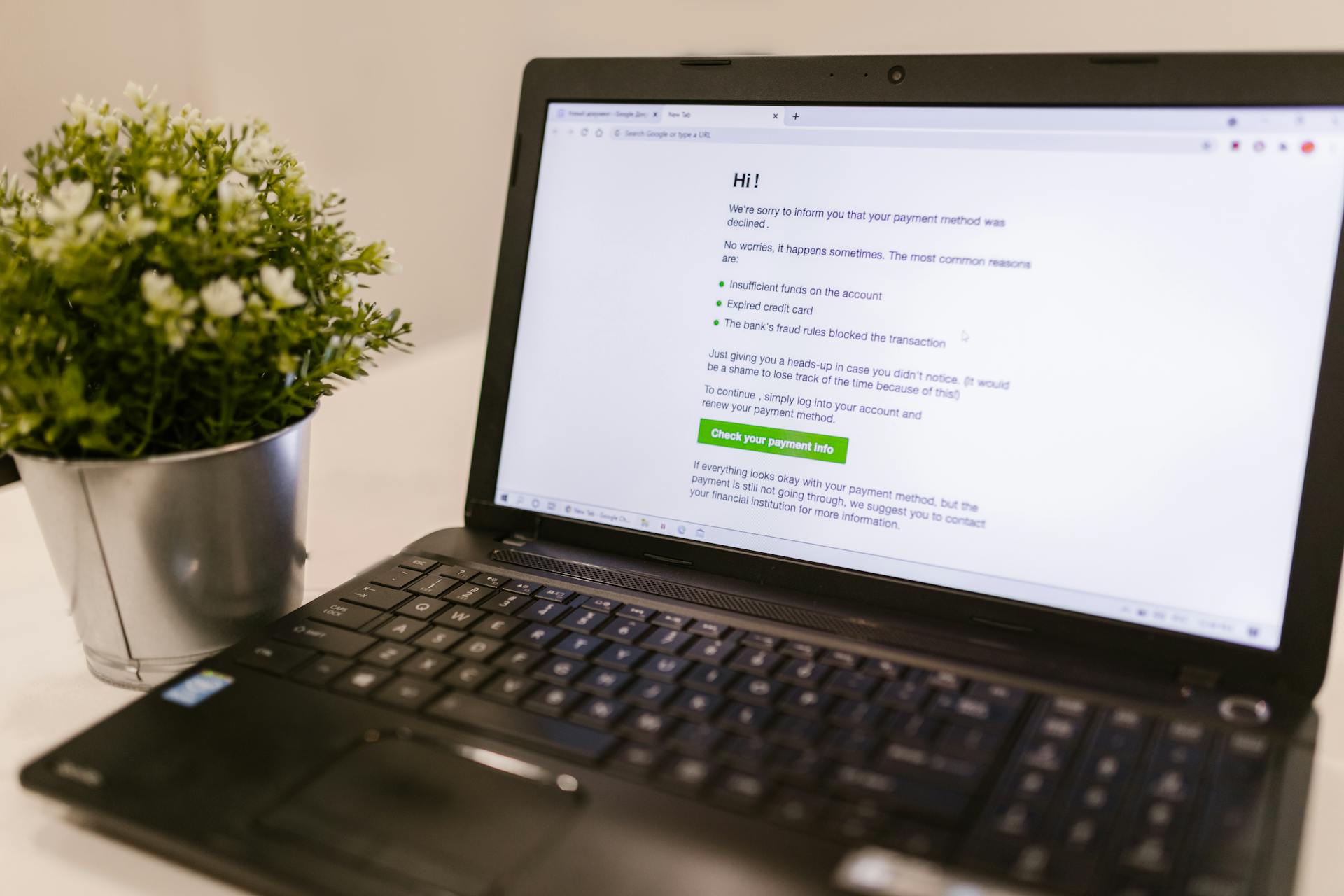 Laptop displaying payment method decline notice alongside a potted plant on a white surface.