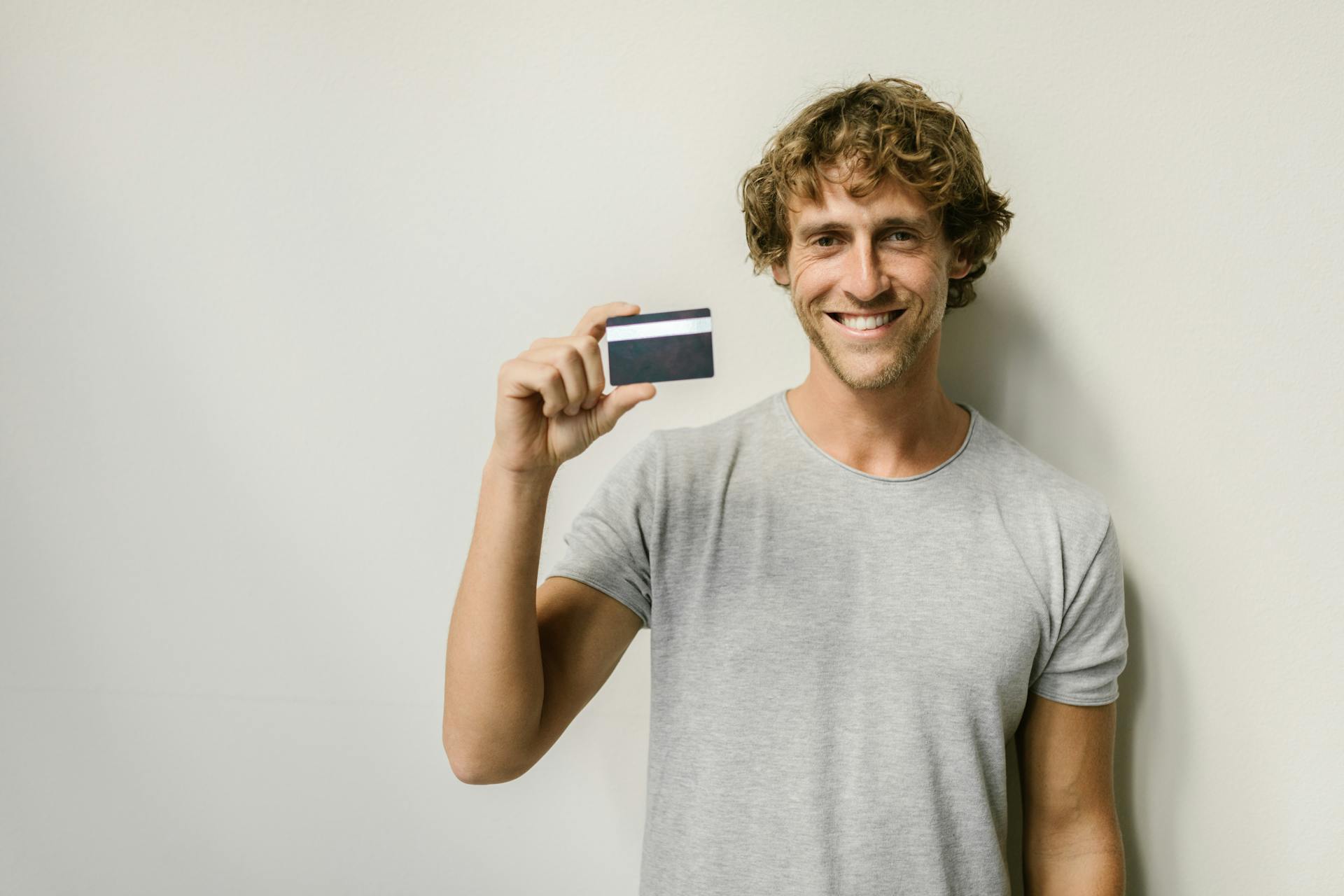 A cheerful man holds a credit card indoors, providing ample copy space for text.