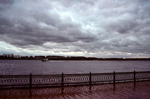 Free Lakeside view with a single boat and dramatic cloudy sky, featuring metal railings. Stock Photo