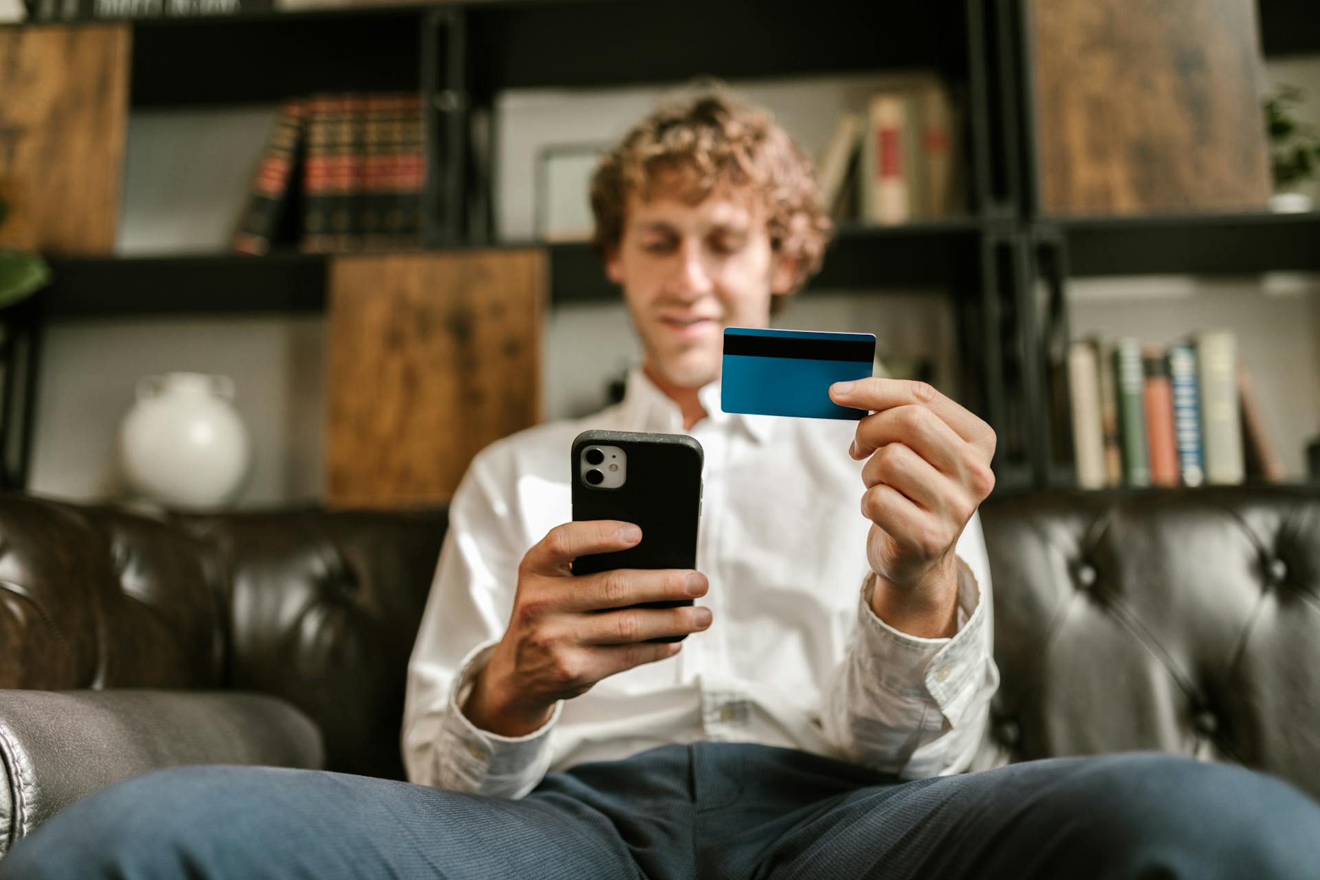 Man in White Long Sleeve Shirt Holding Black Smartphone and Credit Card