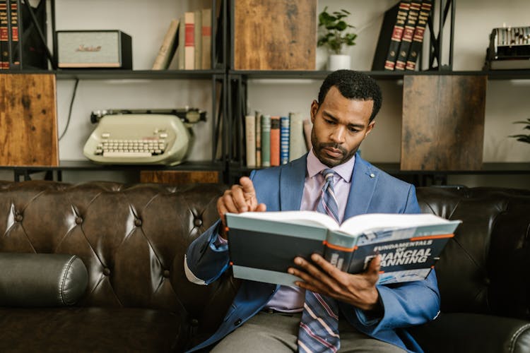 A Man In Corporate Attire Reading A Book On A Couch