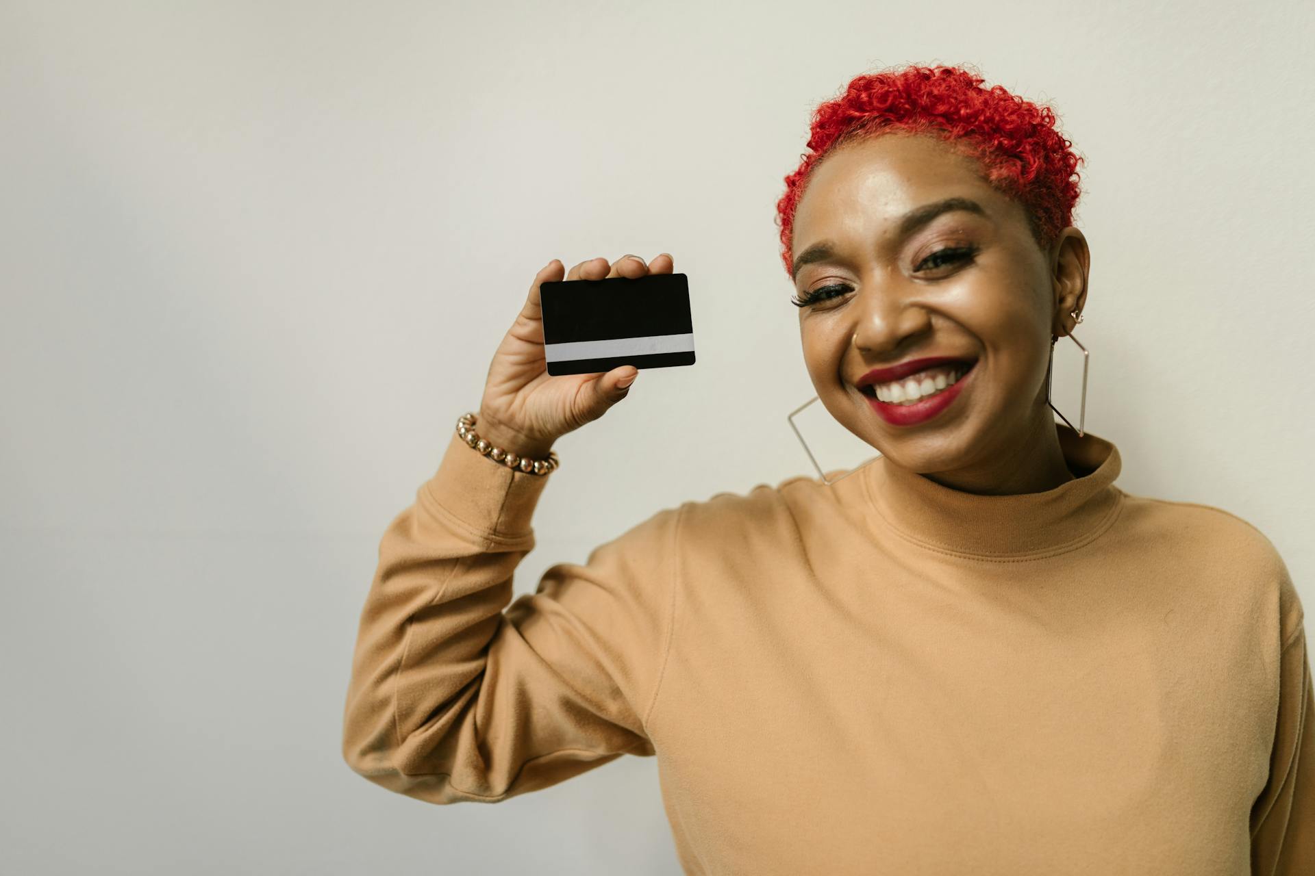 Happy woman with red hair holding a bank card, smiling against a white background.