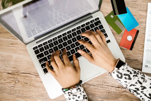 Person typing on a laptop with various credit cards on a wooden desk.