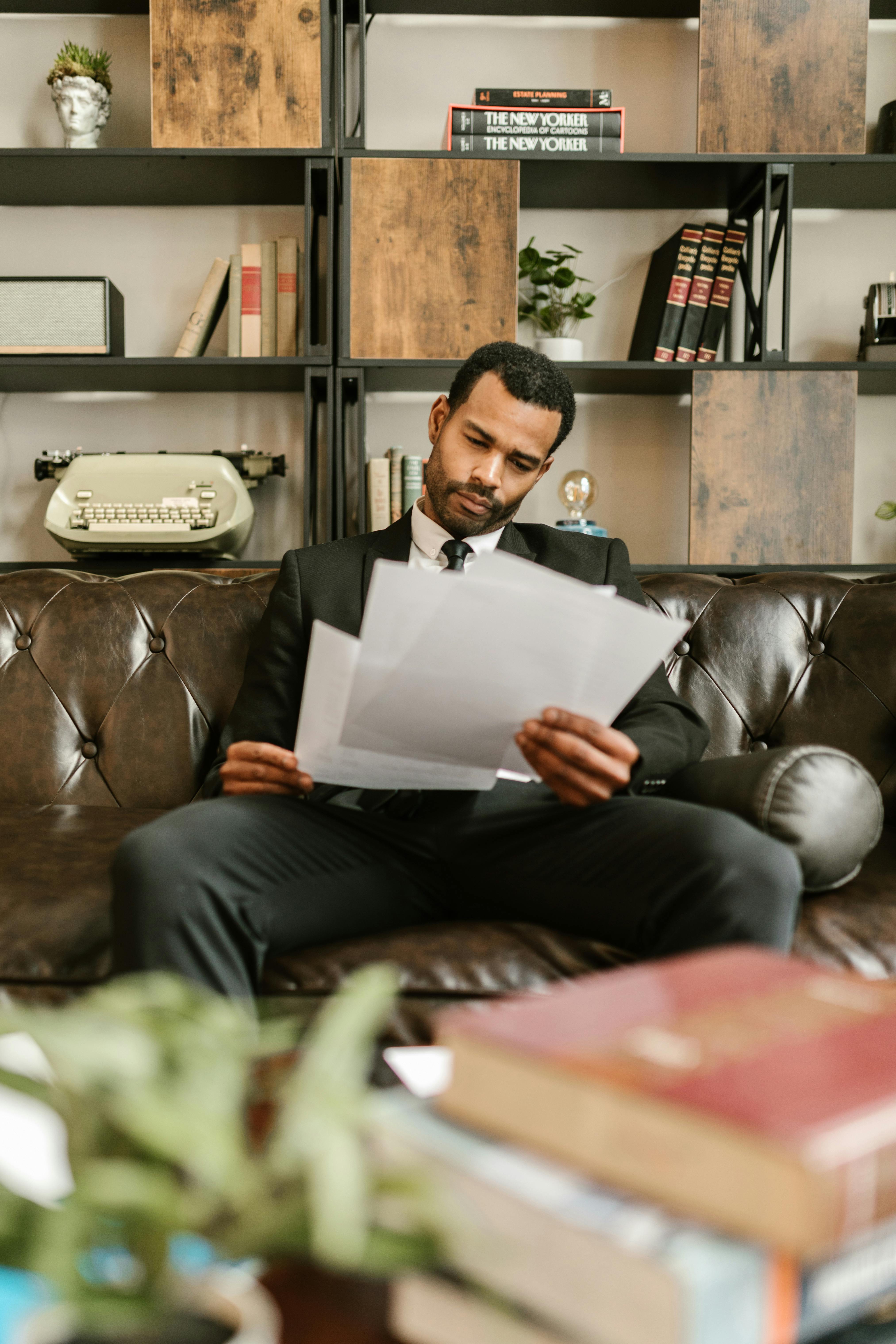 man in black suit sitting on brown leather couch reading documents