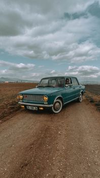 Classic vintage sedan driven on a rural dirt road under a cloudy sky.