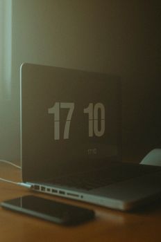 A dimly lit workspace featuring a laptop displaying the time and a smartphone on the table.