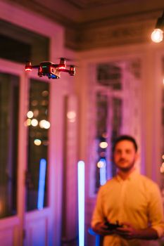 Blurred background of a man controlling a drone indoors with colorful neon lighting.