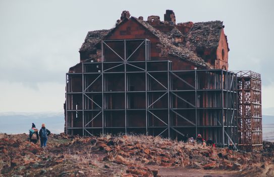 An ancient building structure with scaffolding, surrounded by visitors in a desolate landscape.