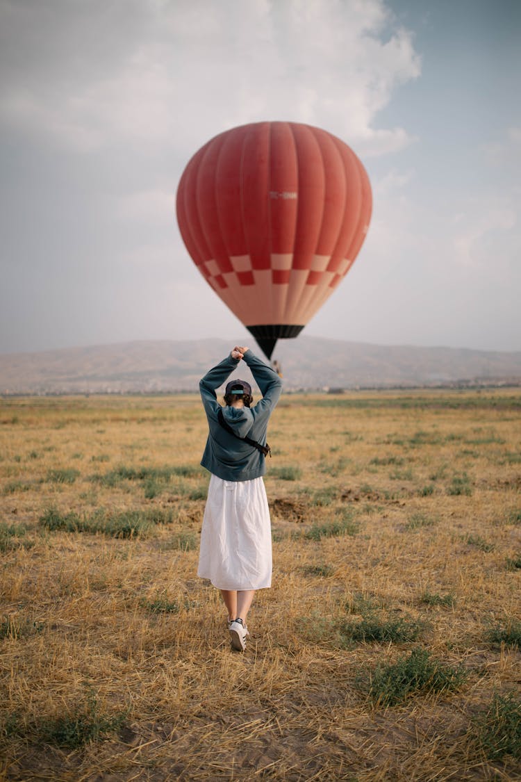 Woman Walking On Grass Field Towards The Hot Air Balloon 