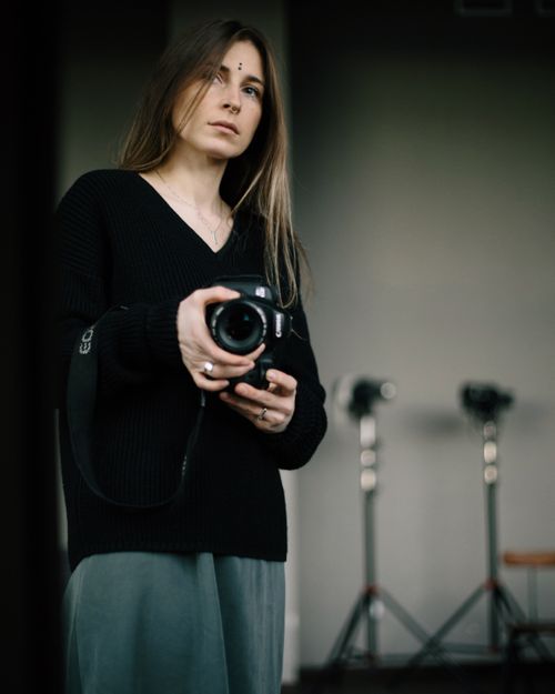 Free Young female photographer in casual clothes standing with professional photo camera in hands and looking away in studio Stock Photo