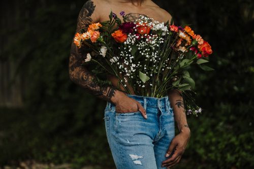 Free Person holding colorful flowers in jeans outdoors, showcasing unique artistic expression. Stock Photo