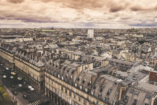 Sweeping aerial view of Paris rooftops showcasing historic architecture under a dramatic sky.