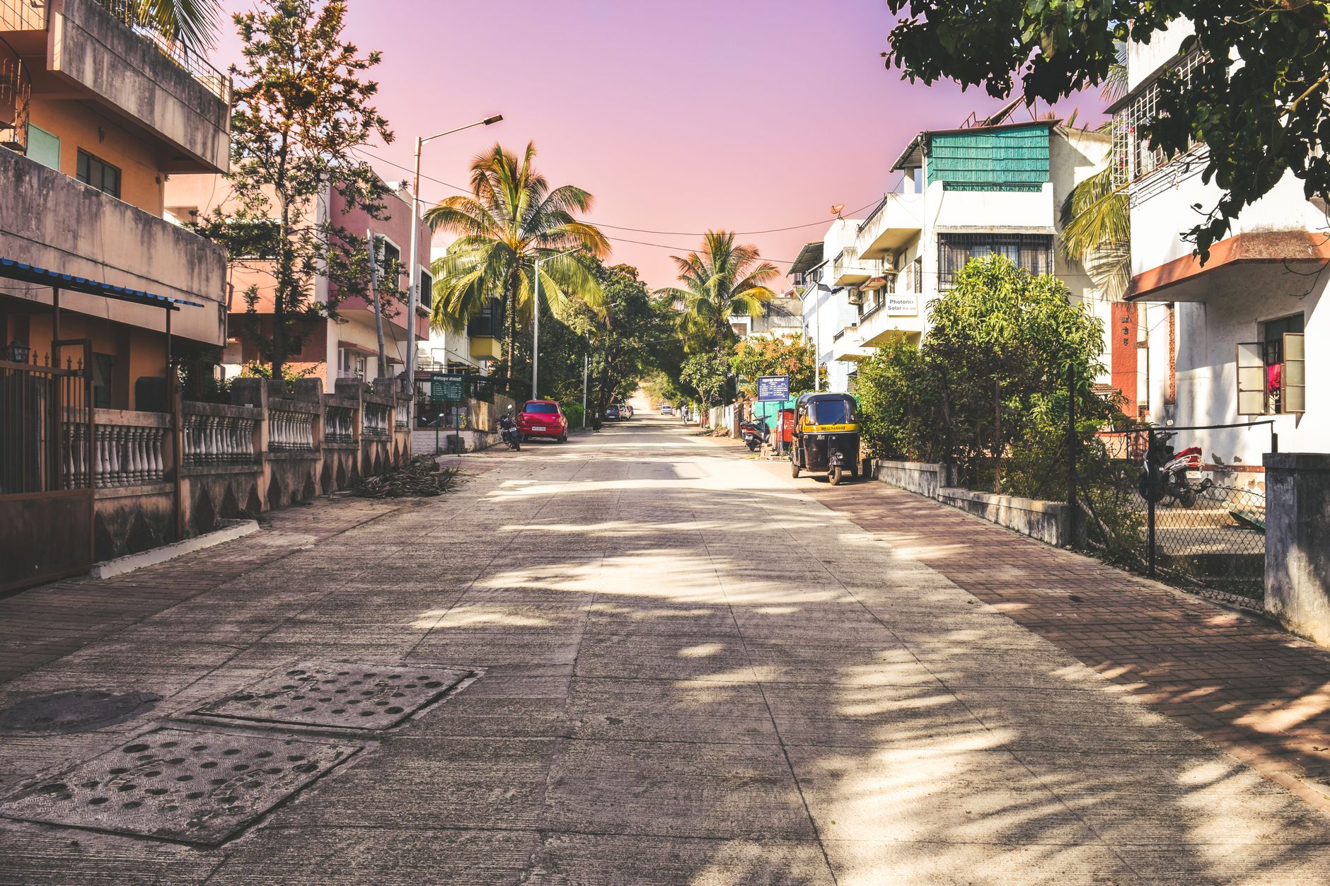 A serene neighborhood street in Pune with palm trees and parked vehicles under a warm sky.