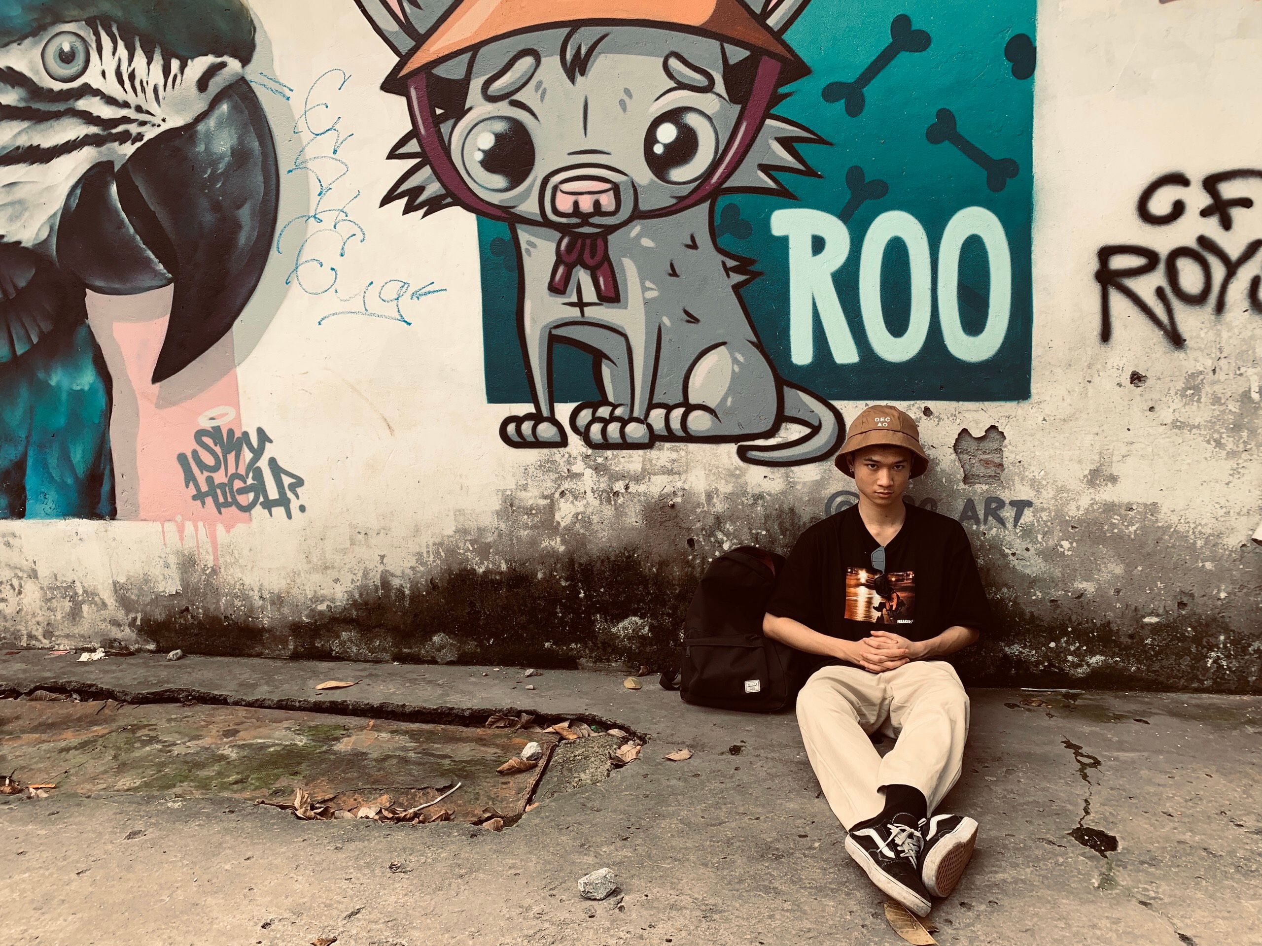 A young man in casual attire sitting by a colorful graffiti wall featuring playful art.