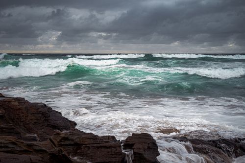 Free Dynamic ocean waves crash against rocky shore at Stanwell Park under cloudy skies. Stock Photo