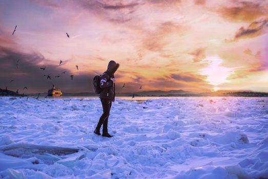 A lone traveler explores a snow-covered landscape as the sun sets, casting vibrant colors in the sky.