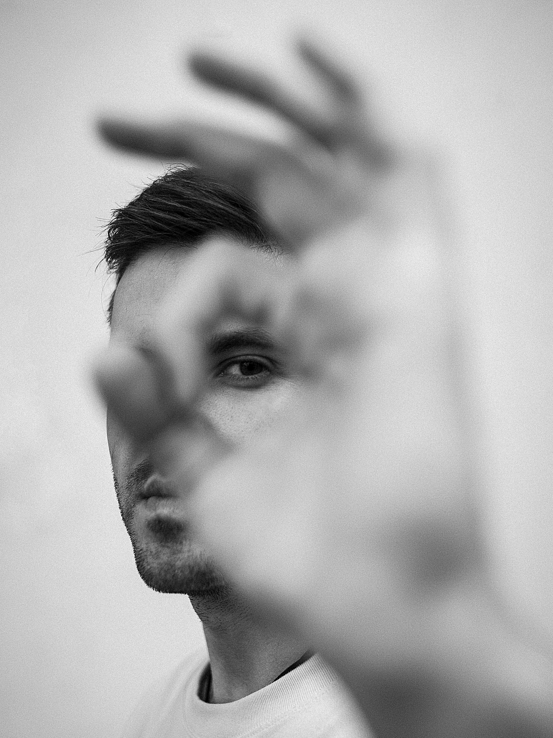 A monochrome portrait of a man with a focus on an abstract hand gesture.